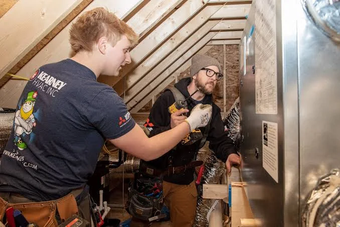 Two technicians working on an indoor attic HVAC air handler
